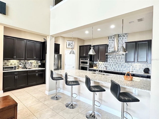 kitchen featuring a breakfast bar area, wall chimney exhaust hood, visible vents, and stainless steel appliances