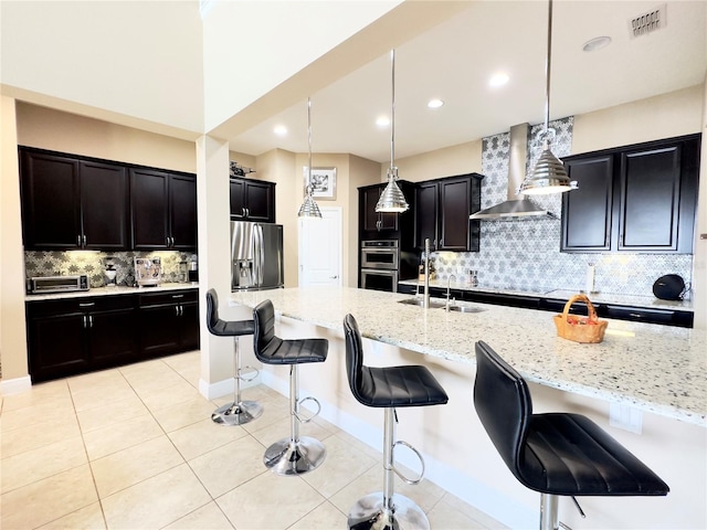 kitchen featuring visible vents, wall chimney range hood, light stone countertops, a breakfast bar area, and appliances with stainless steel finishes