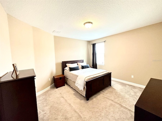 bedroom featuring baseboards, light carpet, a textured ceiling, and visible vents