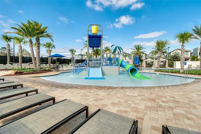 pool with a water slide, fence, a water play area, playground community, and a patio