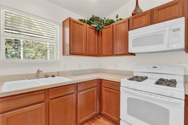 kitchen featuring brown cabinets, white appliances, light countertops, and a sink