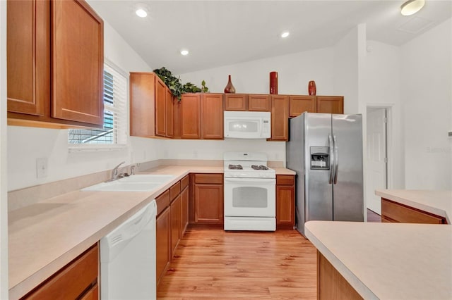 kitchen featuring brown cabinets, vaulted ceiling, a sink, light wood-type flooring, and white appliances