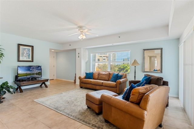 living area featuring light tile patterned floors, a ceiling fan, and baseboards