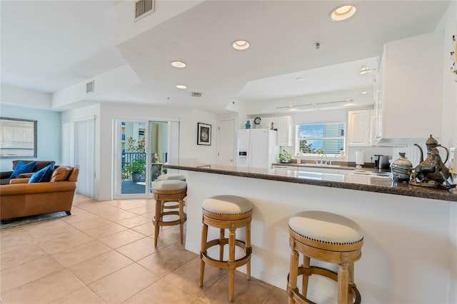 kitchen featuring visible vents, a breakfast bar area, a peninsula, white fridge with ice dispenser, and a sink