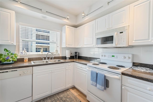 kitchen with white appliances, dark countertops, a sink, and white cabinetry