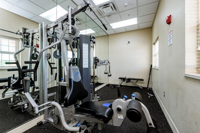 workout area with visible vents, a paneled ceiling, and baseboards