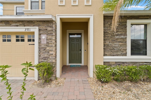 entrance to property featuring stucco siding, stone siding, and a garage