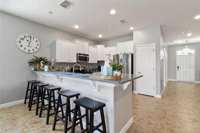 kitchen featuring a breakfast bar, a peninsula, visible vents, and appliances with stainless steel finishes