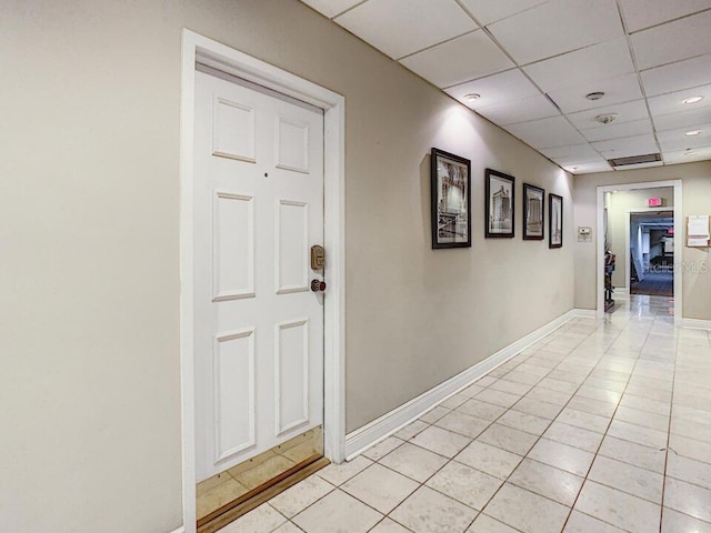 hall featuring a paneled ceiling, light tile patterned flooring, and baseboards