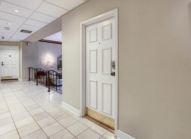 hallway with light tile patterned floors, a drop ceiling, visible vents, and baseboards