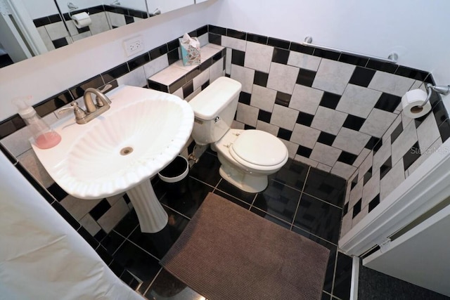 bathroom with toilet, a sink, tile walls, and tile patterned floors