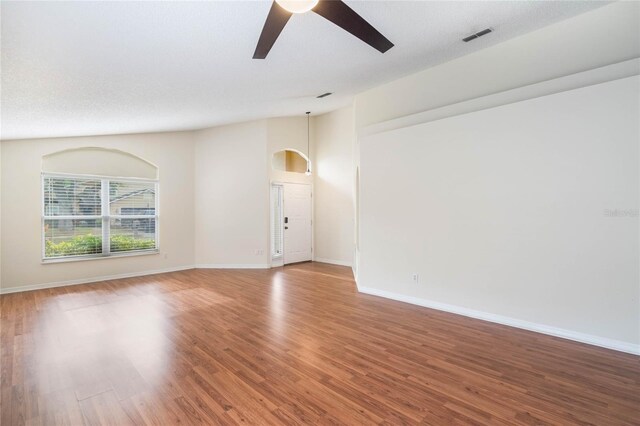 unfurnished room featuring lofted ceiling, wood finished floors, a ceiling fan, visible vents, and baseboards