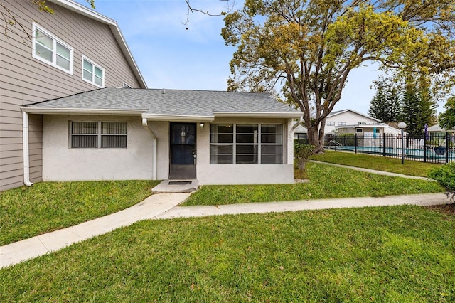 view of front of home with a fenced in pool, stucco siding, a shingled roof, fence, and a front lawn