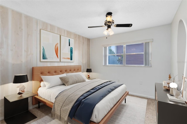 carpeted bedroom featuring arched walkways, wood walls, a ceiling fan, and baseboards