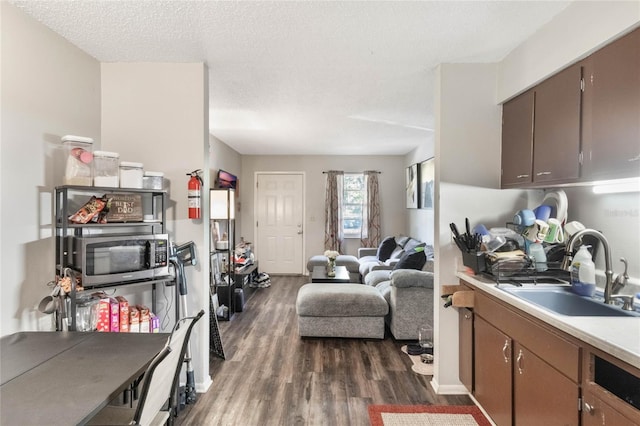 kitchen with dark wood-style floors, stainless steel microwave, open floor plan, a sink, and a textured ceiling