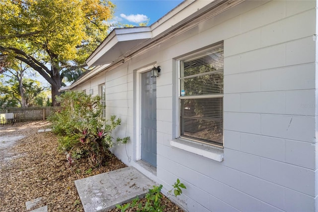 doorway to property featuring concrete block siding and fence