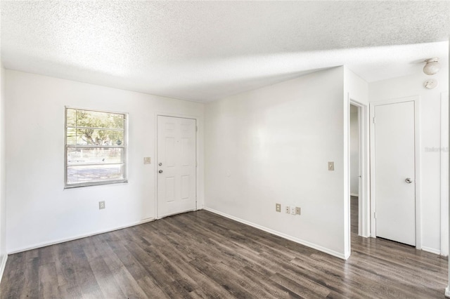 empty room with a textured ceiling, dark wood-type flooring, and baseboards