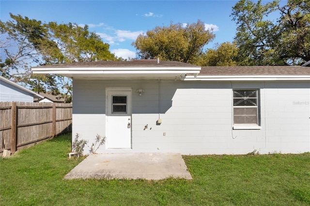 entrance to property featuring concrete block siding, a patio area, a lawn, and fence