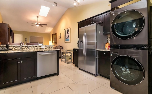 kitchen with a sink, backsplash, stacked washing maching and dryer, stainless steel appliances, and vaulted ceiling with skylight