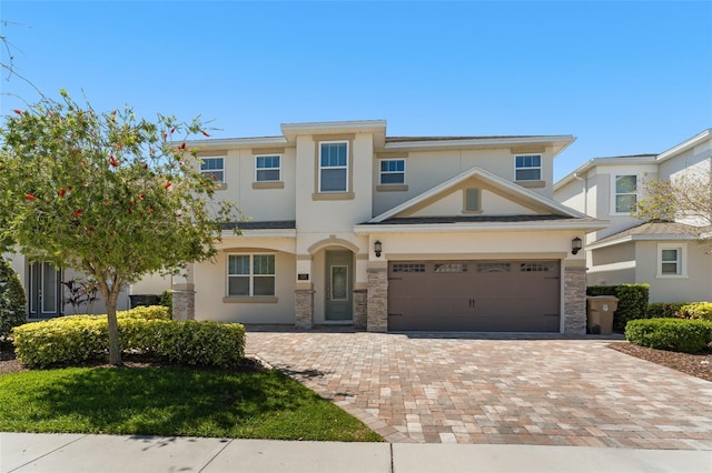 view of front facade featuring decorative driveway, stone siding, an attached garage, and stucco siding