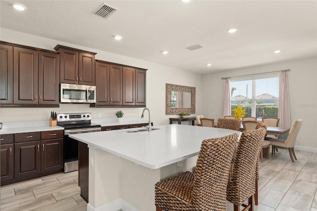 kitchen with a center island with sink, visible vents, a sink, light countertops, and appliances with stainless steel finishes