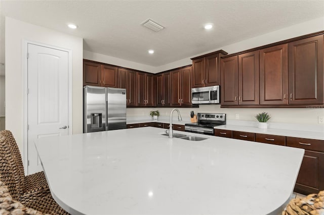 kitchen with visible vents, a sink, light countertops, stainless steel appliances, and a kitchen island with sink