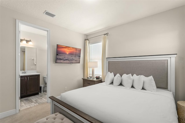 bedroom with baseboards, visible vents, a sink, light carpet, and connected bathroom