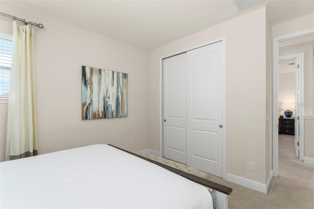 bedroom featuring baseboards, visible vents, a closet, a textured ceiling, and light colored carpet