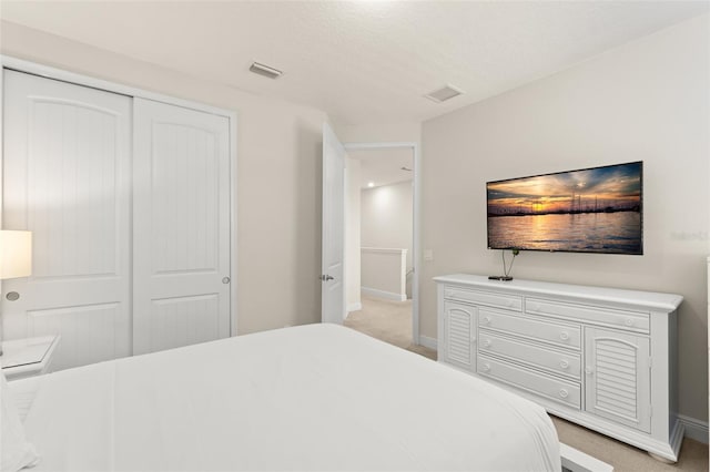 bedroom featuring a closet, visible vents, light colored carpet, and baseboards