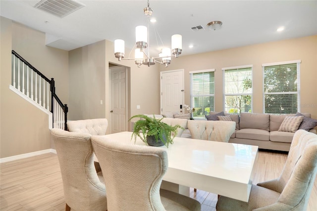 dining area with a chandelier, light wood-type flooring, visible vents, and stairway