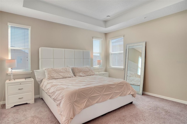 bedroom featuring baseboards, a tray ceiling, and light colored carpet