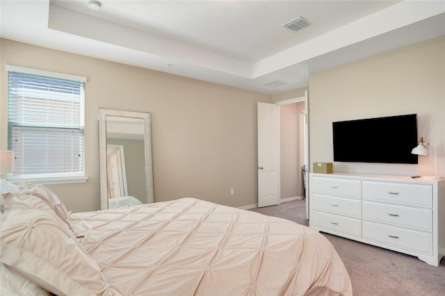 bedroom with baseboards, visible vents, a tray ceiling, and light colored carpet