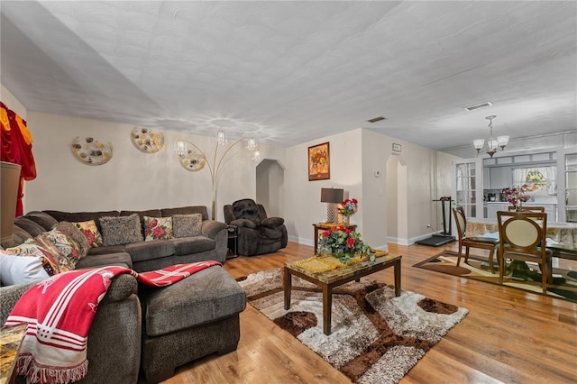 living area with a chandelier, visible vents, light wood-style flooring, and arched walkways