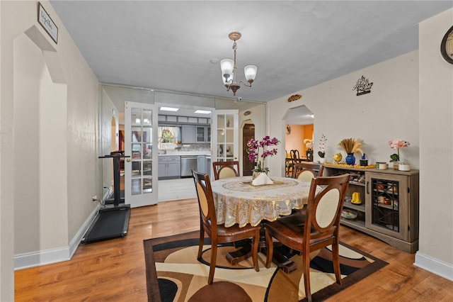 dining area featuring arched walkways, an inviting chandelier, baseboards, and light wood-style floors