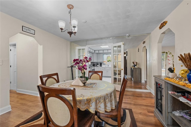 dining space featuring arched walkways, a notable chandelier, baseboards, and wood finished floors