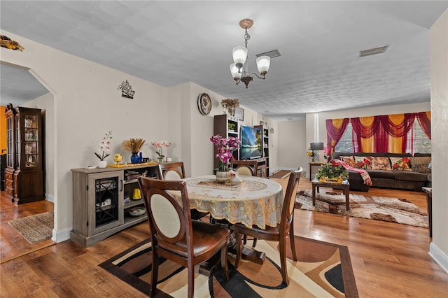 dining area featuring arched walkways, visible vents, an inviting chandelier, and wood finished floors