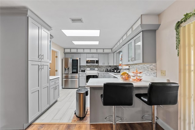 kitchen with gray cabinetry, light countertops, decorative backsplash, appliances with stainless steel finishes, and a peninsula