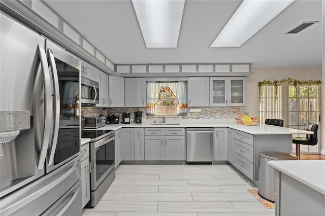 kitchen with visible vents, appliances with stainless steel finishes, a peninsula, and gray cabinetry