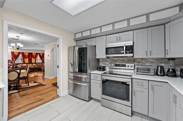 kitchen with a chandelier, light countertops, decorative backsplash, gray cabinets, and appliances with stainless steel finishes