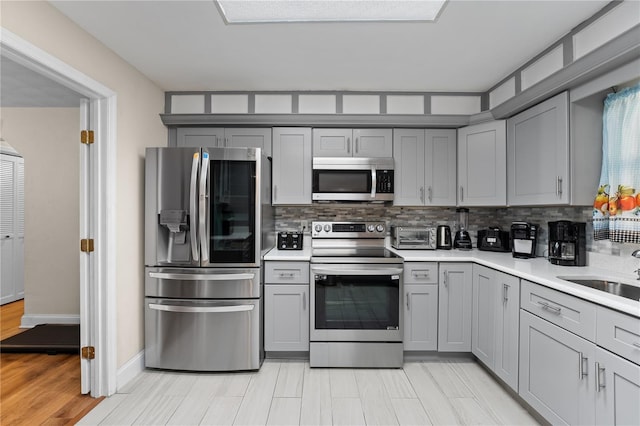 kitchen with tasteful backsplash, gray cabinetry, light countertops, appliances with stainless steel finishes, and a sink