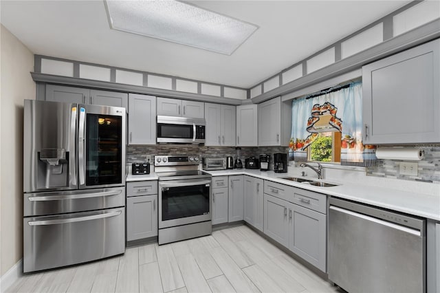 kitchen featuring light countertops, decorative backsplash, gray cabinets, appliances with stainless steel finishes, and a sink