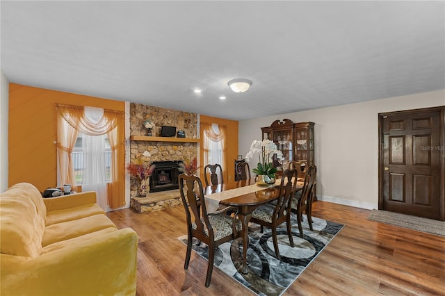 dining space with a stone fireplace, baseboards, and light wood finished floors