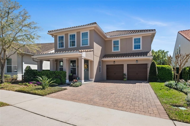 mediterranean / spanish-style home featuring a tile roof, decorative driveway, an attached garage, and stucco siding