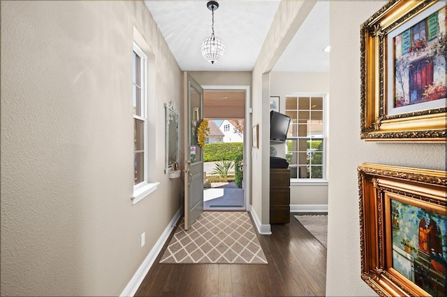 entryway with dark wood finished floors, a notable chandelier, and baseboards