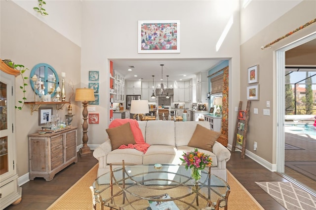 living area featuring a notable chandelier, baseboards, a towering ceiling, and wood finished floors