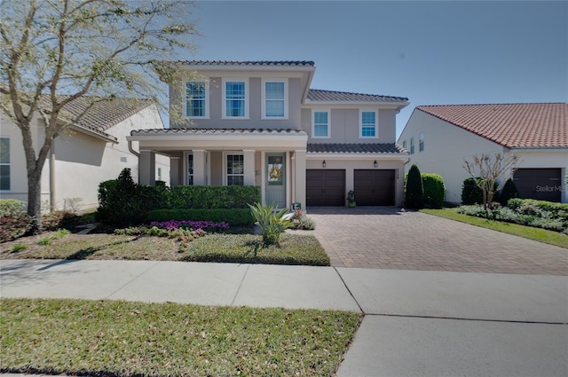 mediterranean / spanish-style house featuring a tile roof, decorative driveway, a garage, and stucco siding