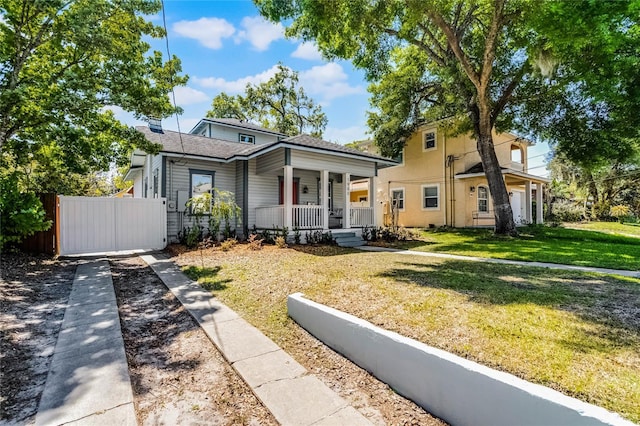 bungalow featuring covered porch, a shingled roof, a front lawn, and fence