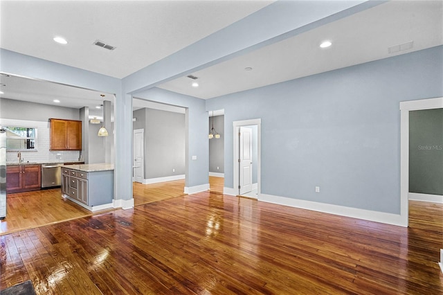 unfurnished living room featuring visible vents, baseboards, recessed lighting, a sink, and light wood-type flooring