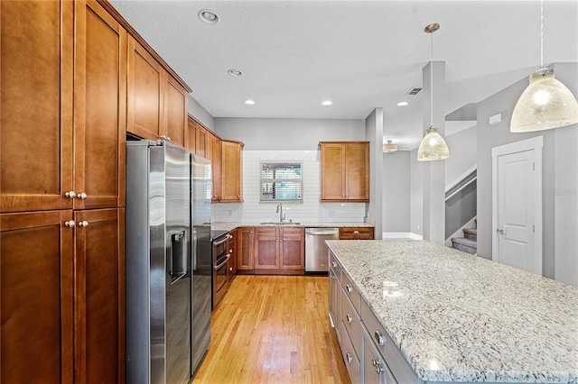 kitchen featuring light wood-style flooring, a sink, light stone counters, stainless steel appliances, and decorative backsplash