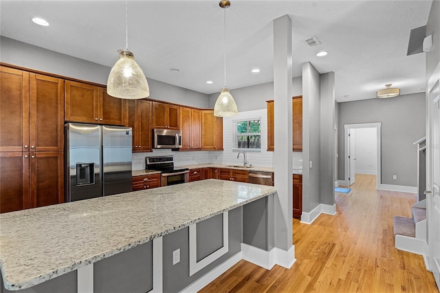 kitchen with a sink, stainless steel appliances, light wood-style floors, decorative backsplash, and light stone countertops